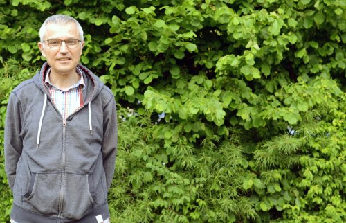 Claus Werninger steht vor einer grünen Hecke.