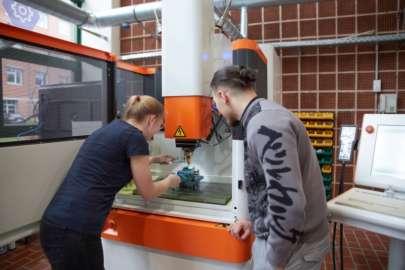 Zwei Studierende arbeiten an einem großen Standbohrer.